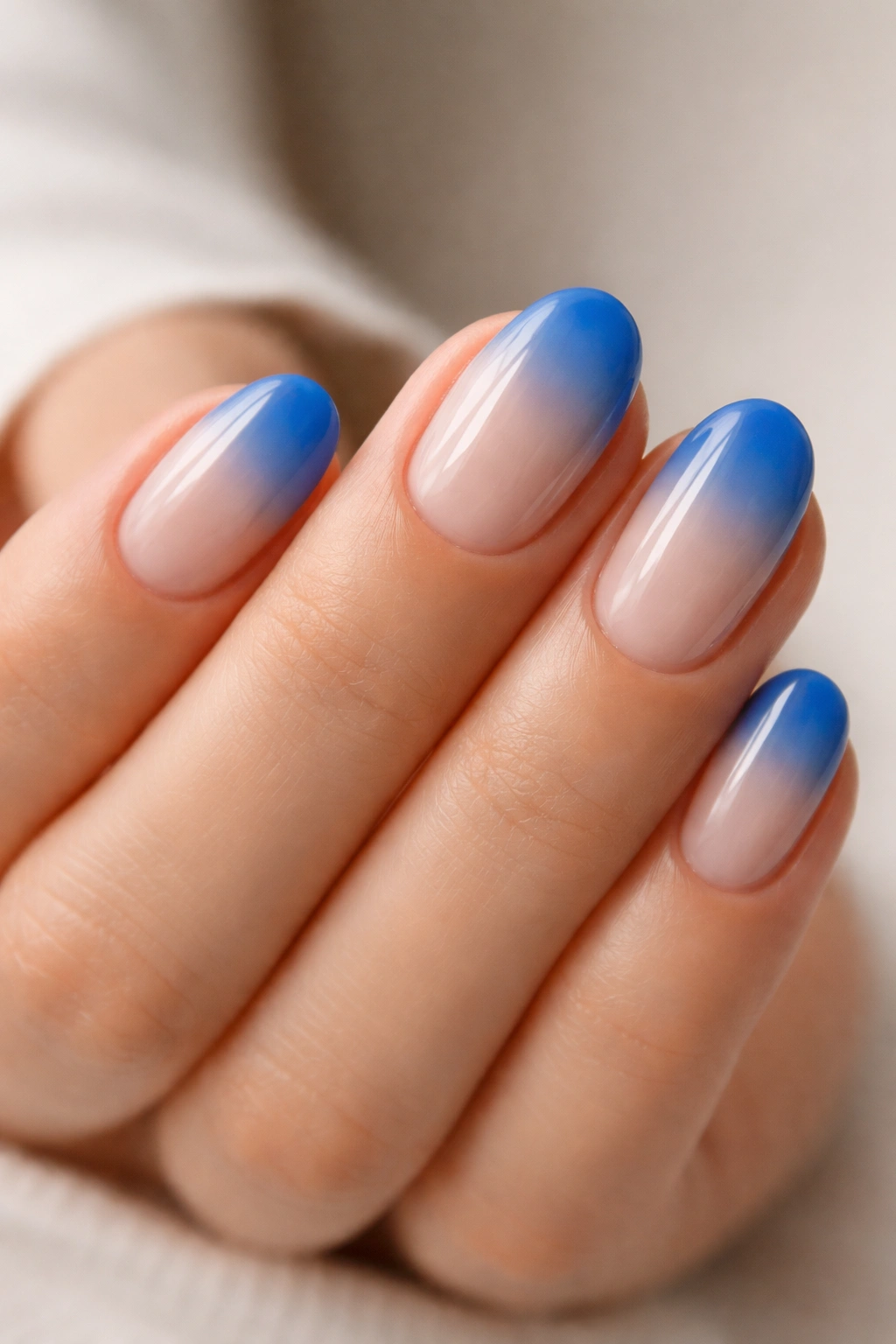 Close-up of short oval nails painted electric blue with a milky base
