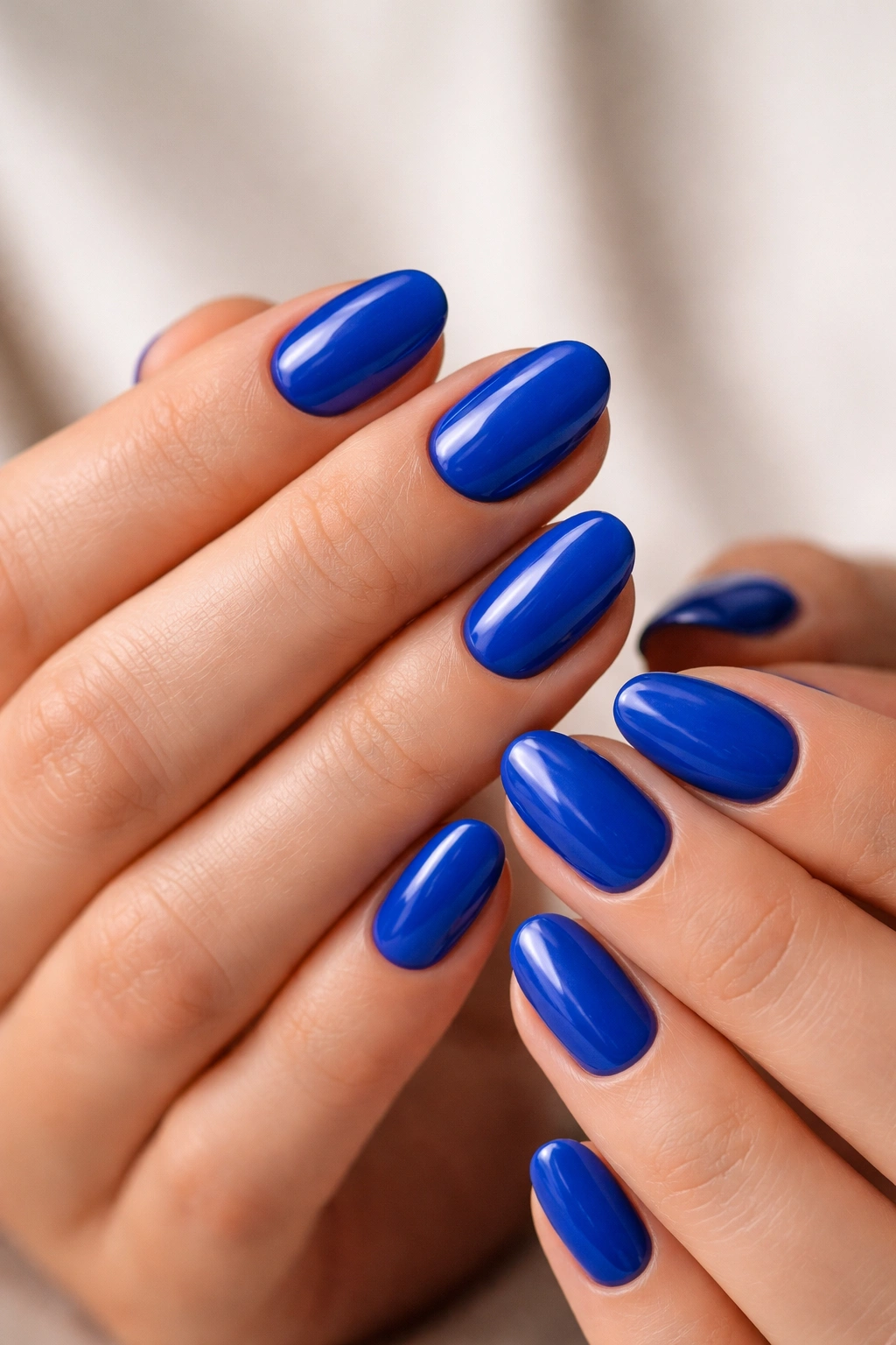 Close-up of short oval nails in electric cobalt blue with a glossy finish