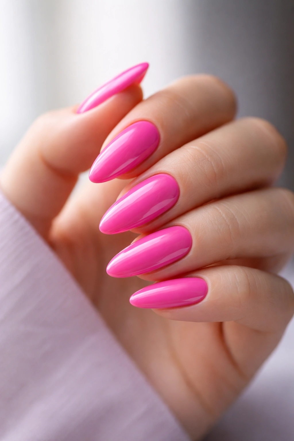 Close-up of electric pink almond nails with cool undertone and glossy finish on a bare hand