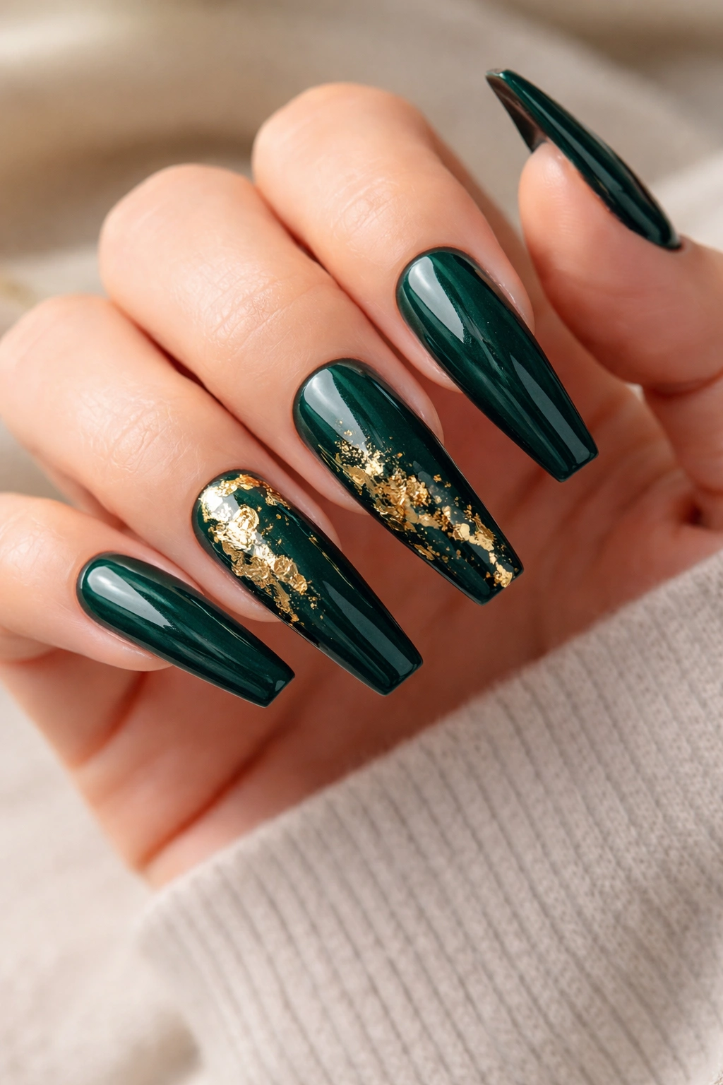 Close-up of long coffin nails in deep emerald green with gold foil accents