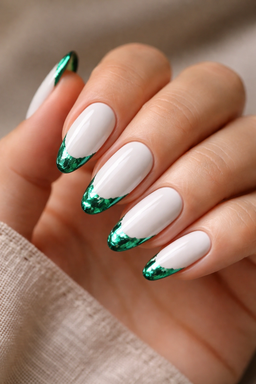 Close-up of white almond nails with emerald green foil tips