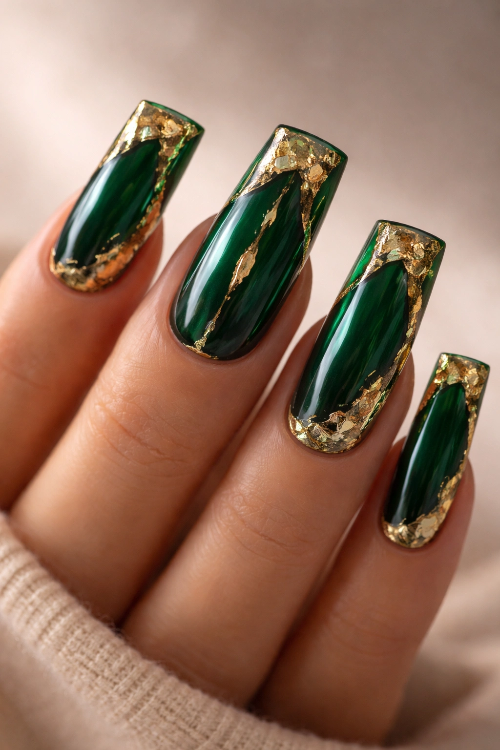 Close-up of emerald green duck nails with gold foil accents on a hand in a neutral studio setting