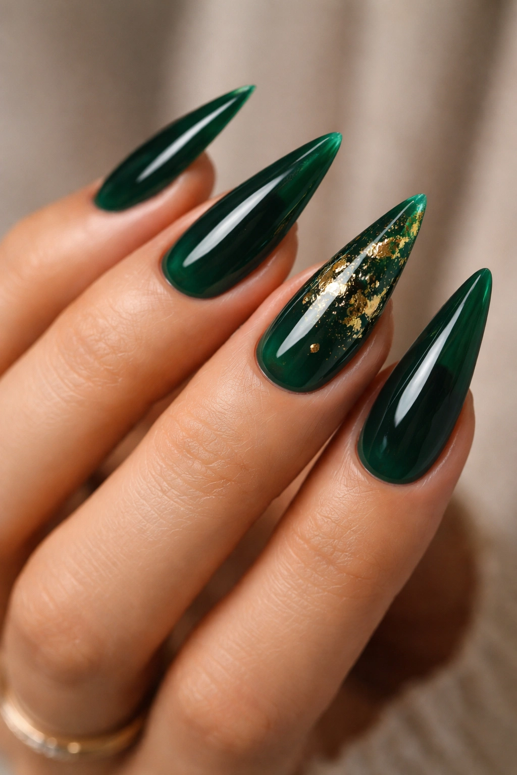 Close-up of emerald green stiletto nails with gold foil accents