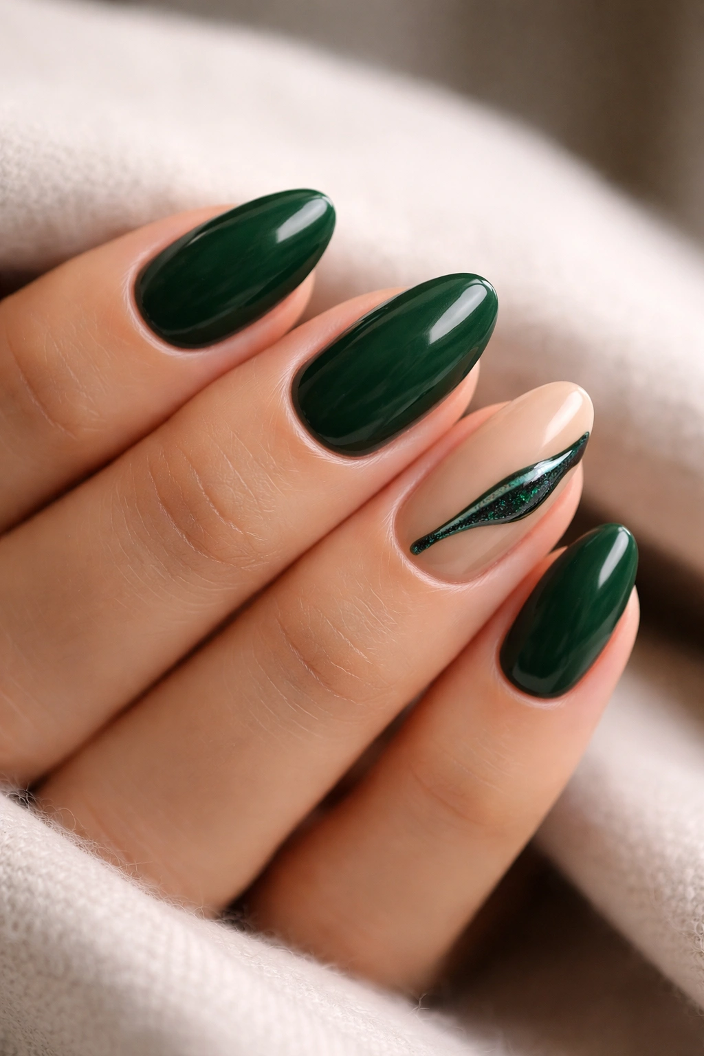 Close-up of short almond nails in deep emerald green with one nude accent nail featuring a fine emerald line