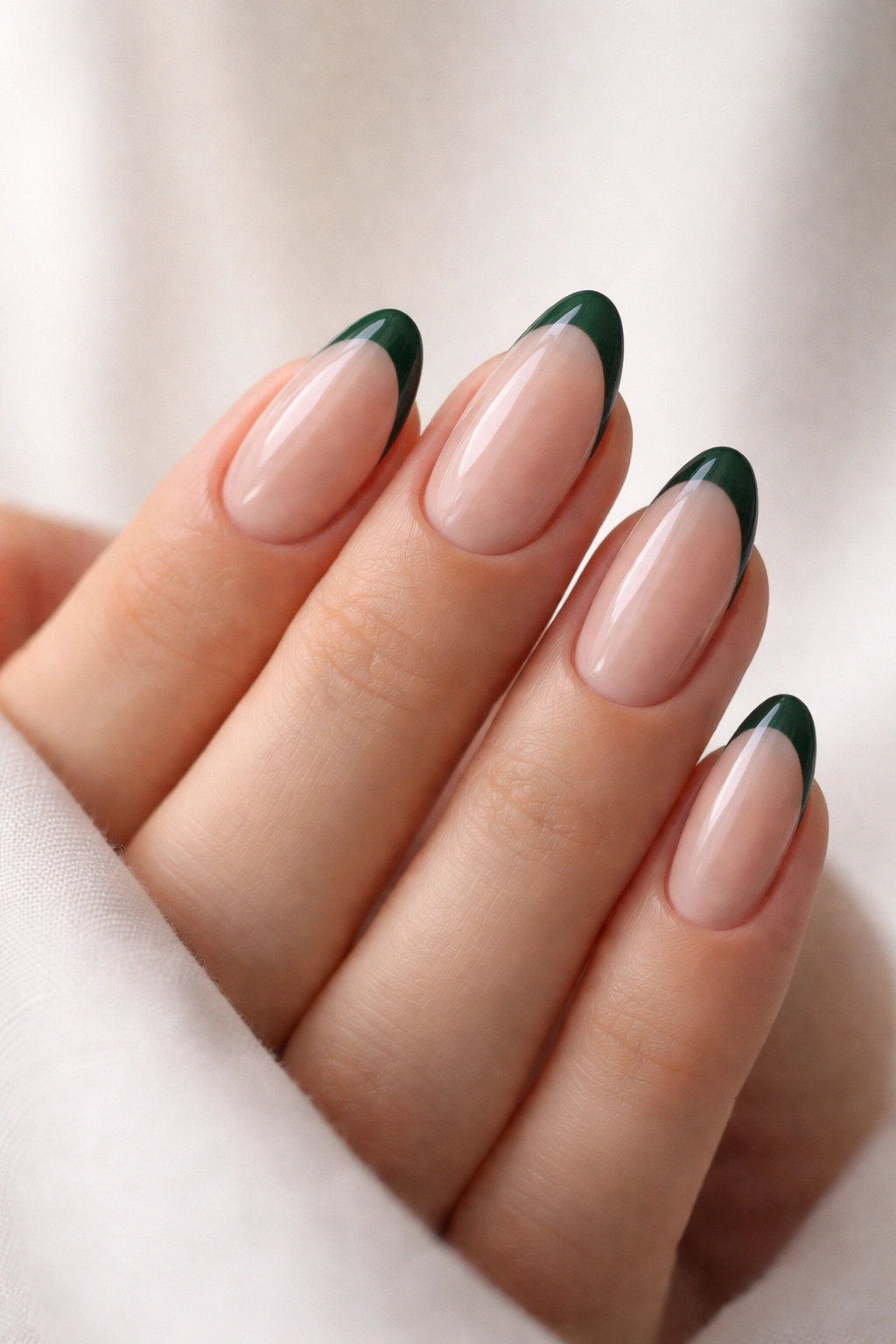 Close-up of short almond nails with nude base and emerald tips