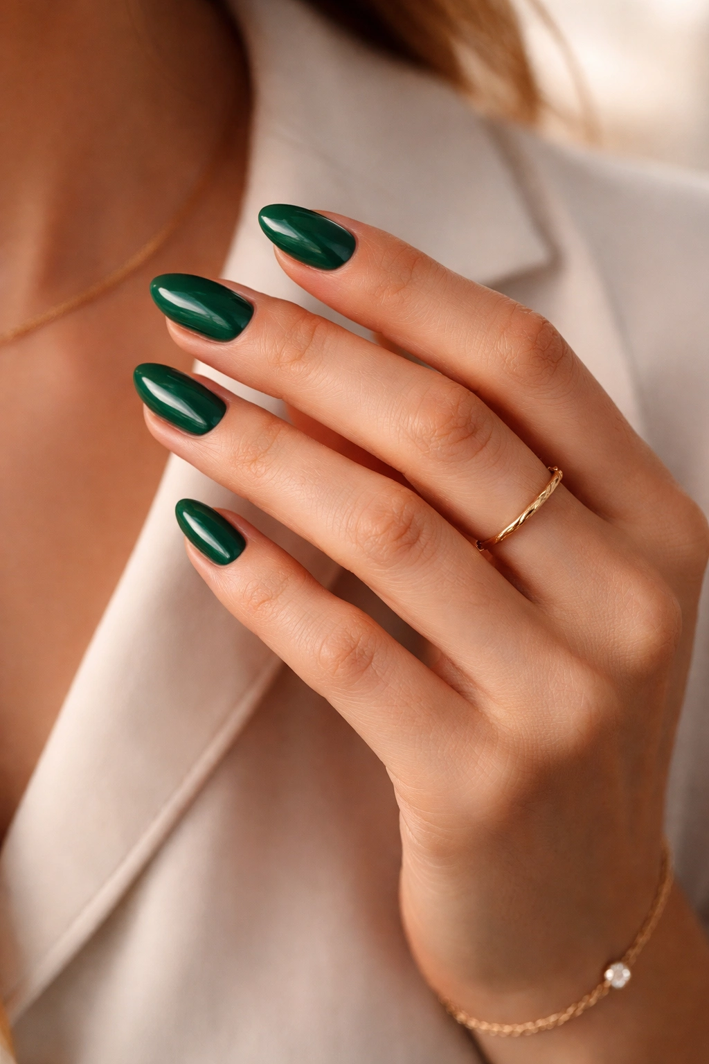 Emerald nails paired with gold jewelry on a hand against a neutral background