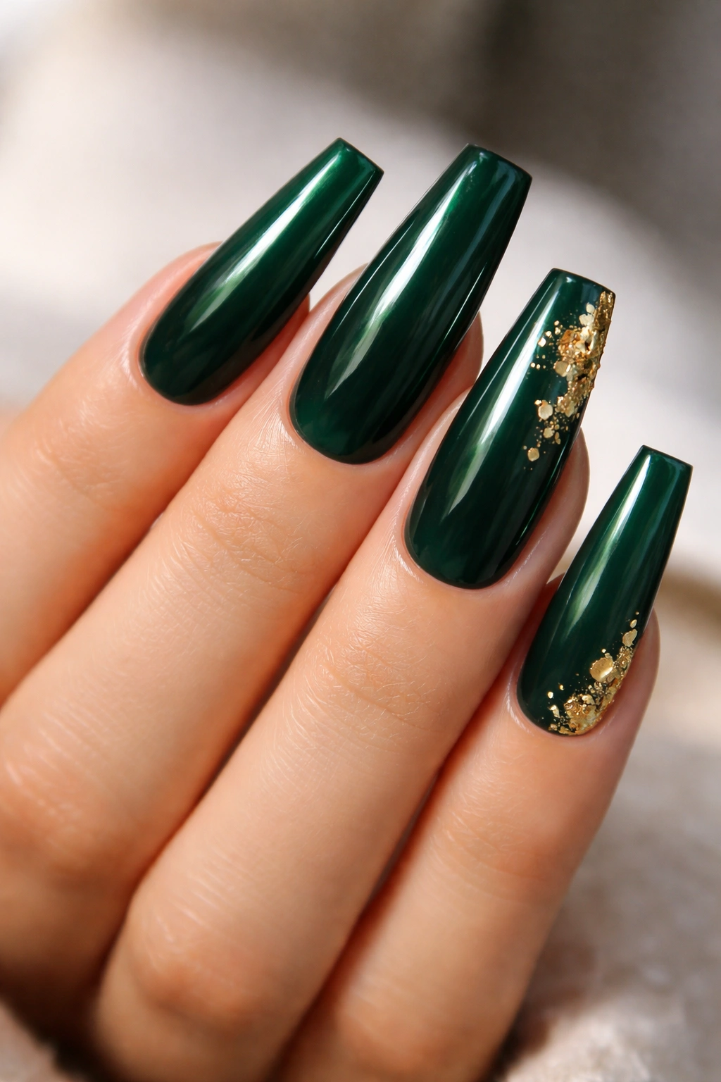 Close-up of deep emerald coffin nails with gold leaf accents on a neutral background