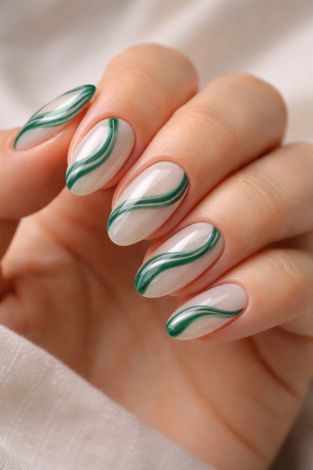 Close-up of short almond nails featuring emerald and milky white swirls with negative space