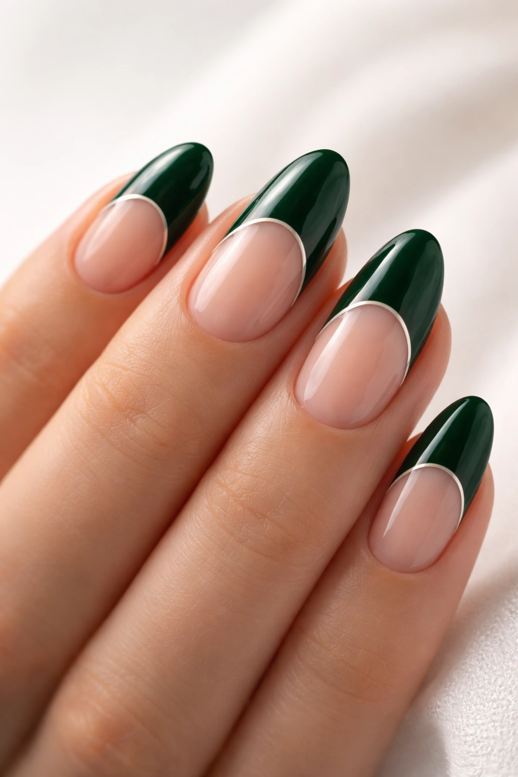 Close-up of short almond nails with dark emerald tips and negative space crescent arc