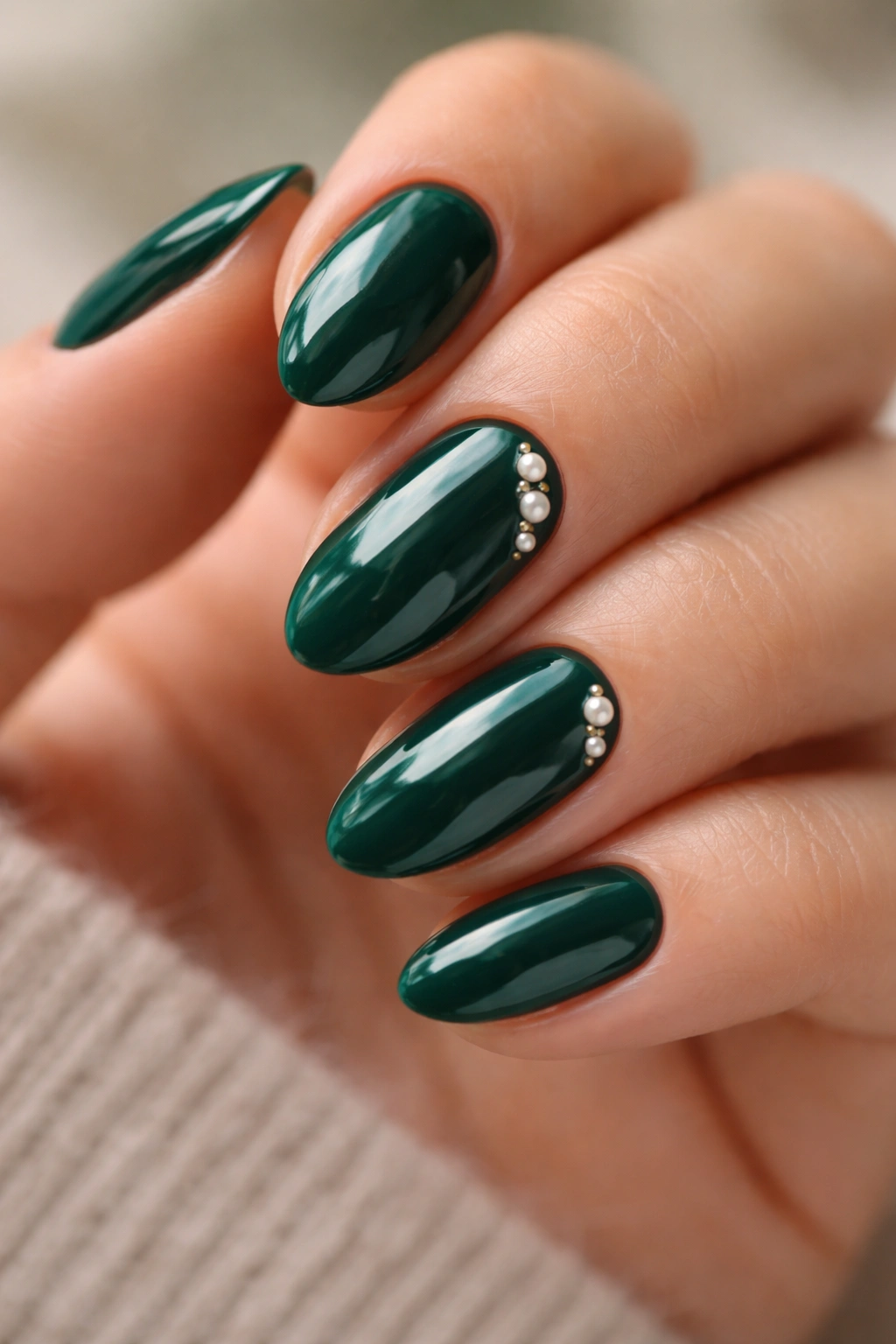 Short almond nails with tiny pearl accents on emerald polish
