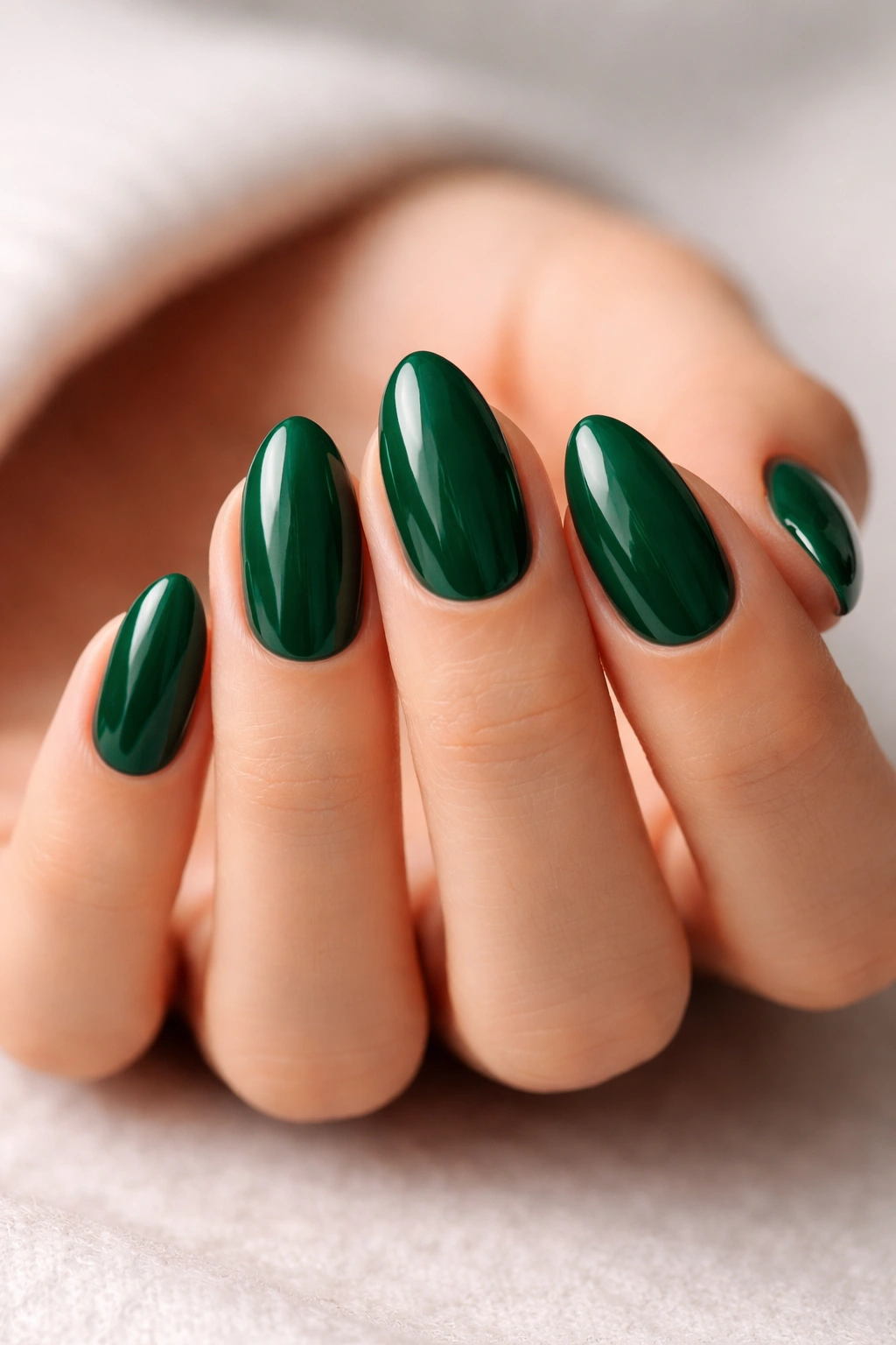 Close-up of short almond nails in high-gloss emerald green