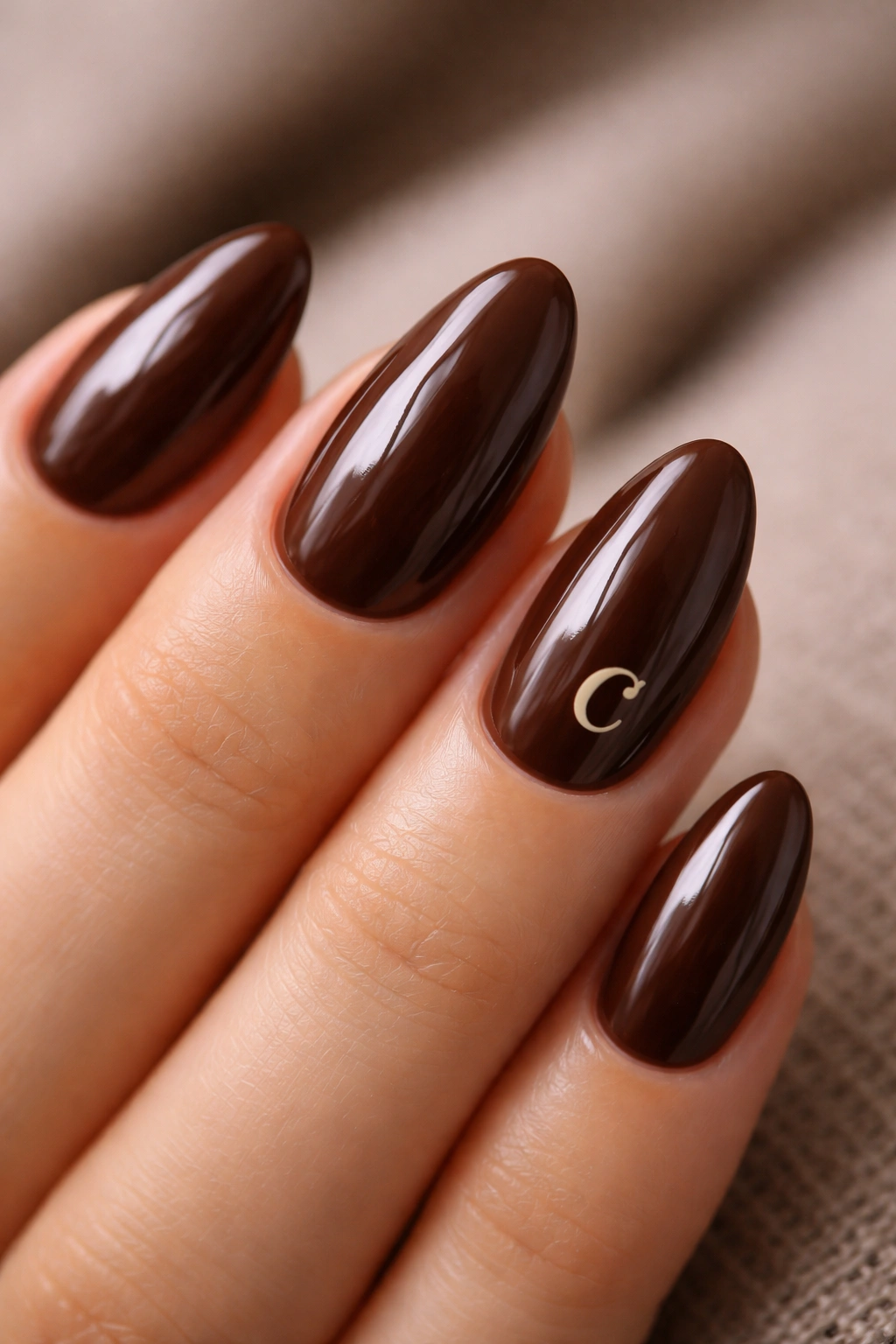 Close-up of espresso brown short almond nails with a cream monogram mark