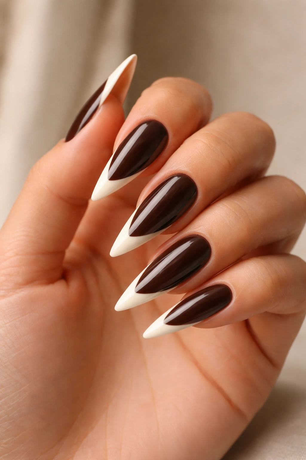 Close-up of espresso brown stiletto nails with lighter cream French tips on a hand.