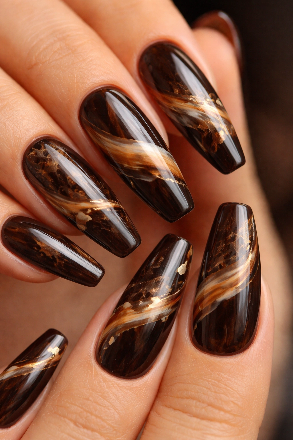 Close-up of espresso agate marble nails with caramel ribbons and gold accents