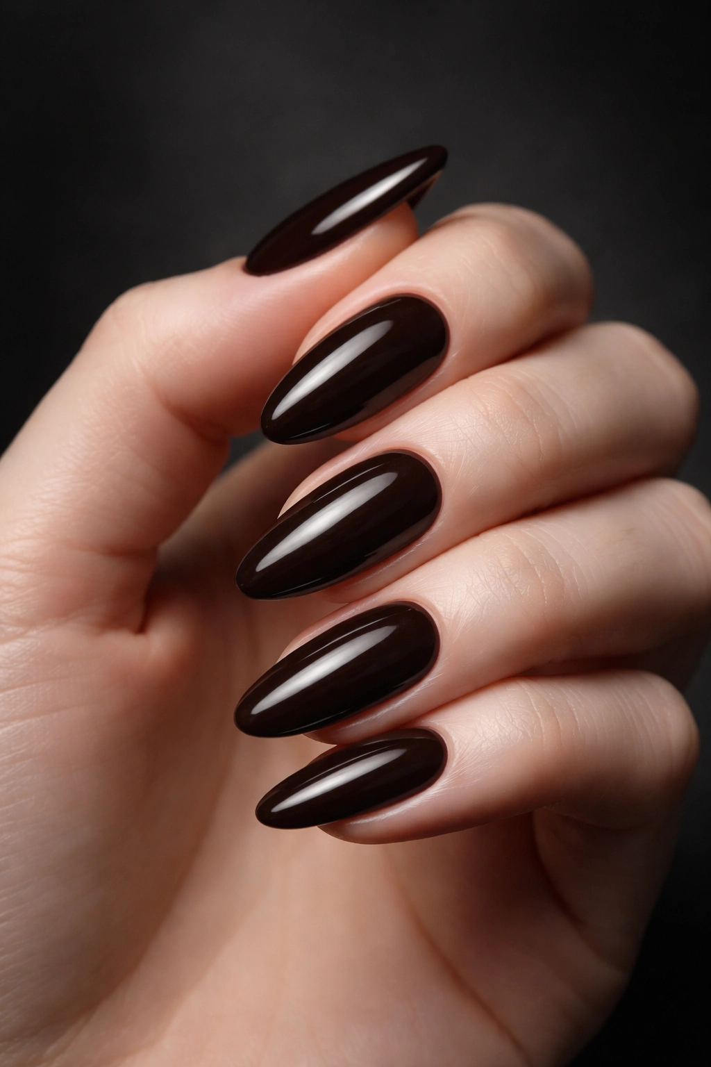 Pale-skinned hand with deep espresso nails against charcoal background