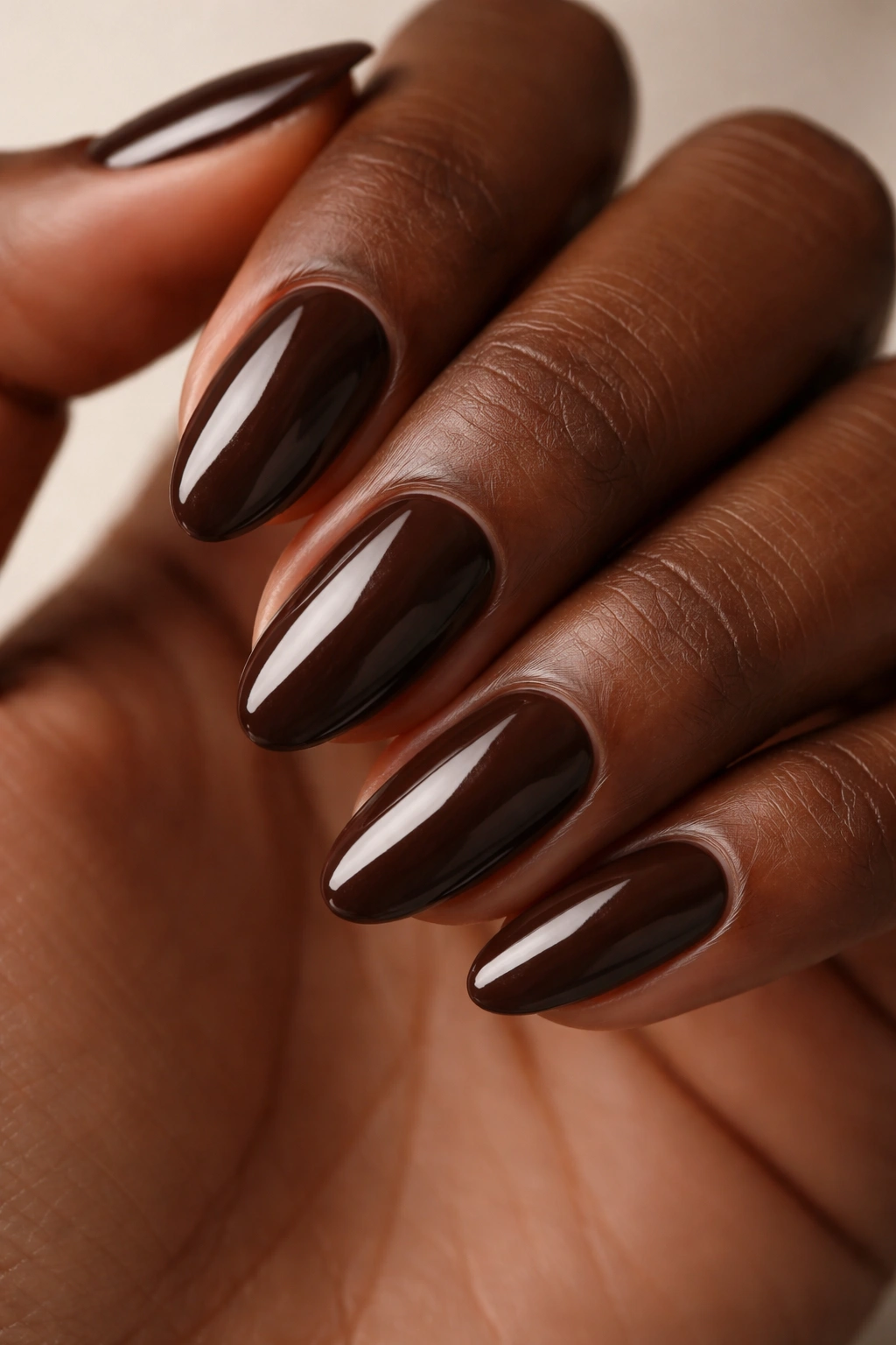 Close-up of short almond nails in deep espresso glossy brown on dark skin