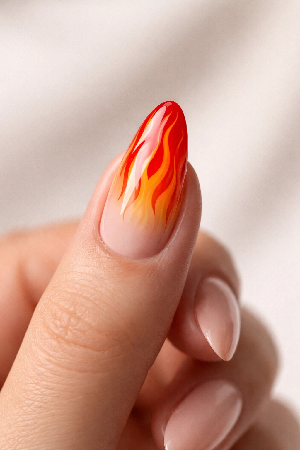 Close-up of a hand with a single flame nail against neutral background