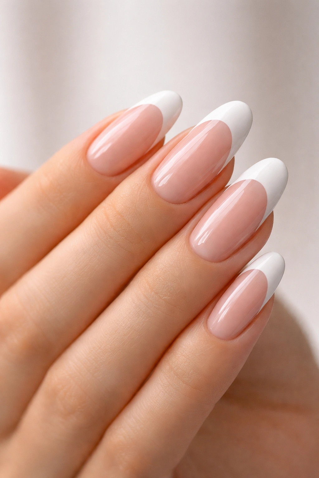 Close-up of long round French nails with white tips on a single hand with a neutral backdrop