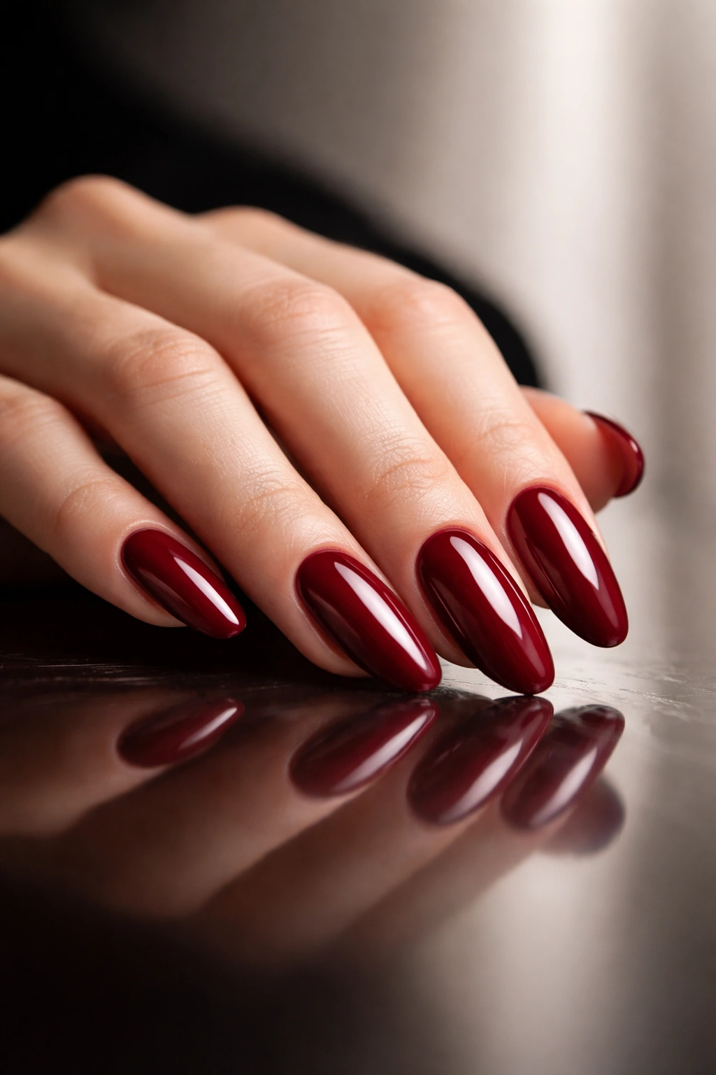 Close-up of deep red nails on a hand with reflective surface