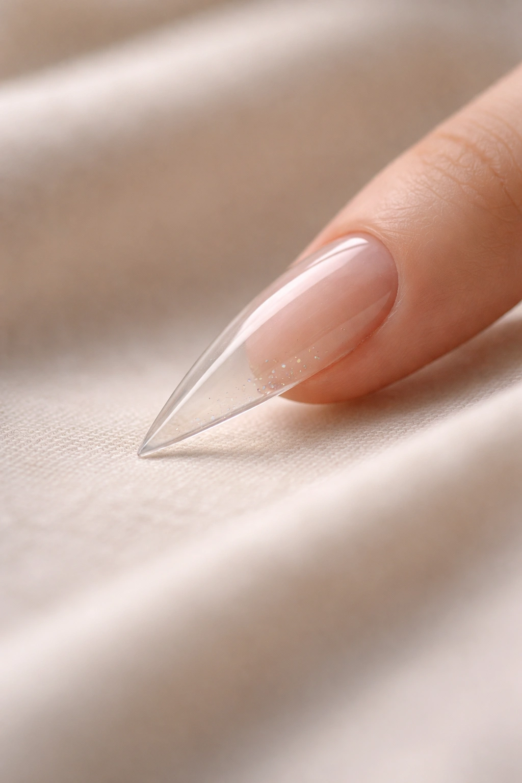 Minimalist close-up of a clear stiletto nail on a soft surface