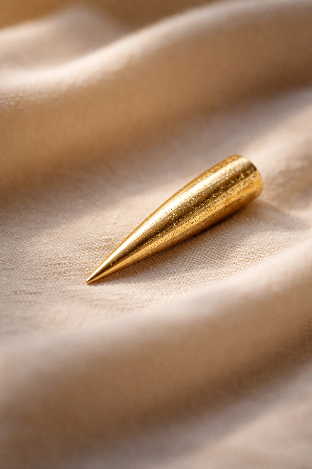 Single gold-stiletto nail on neutral fabric in a contemplative still-life