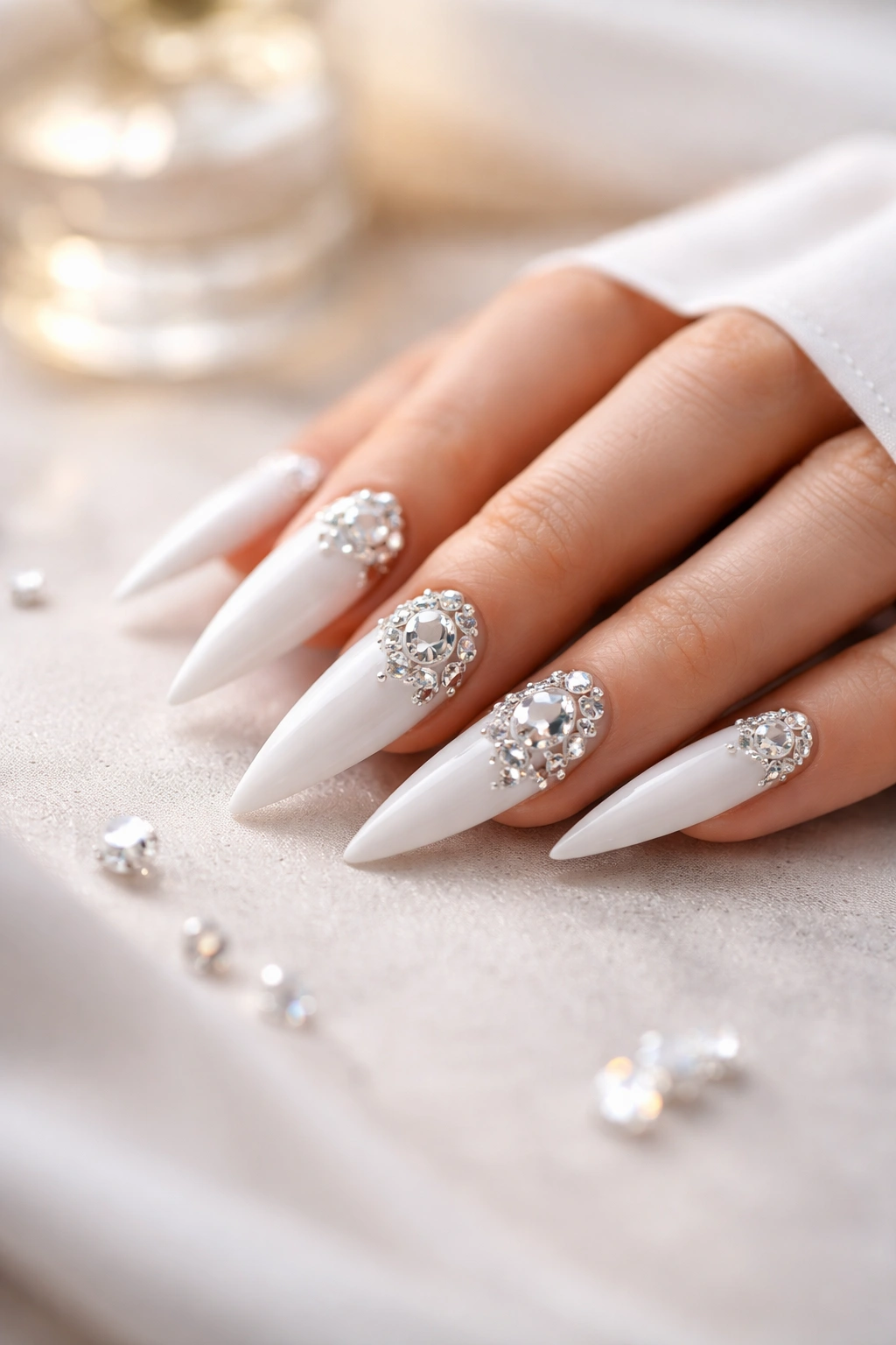 Close-up of white stiletto nails with rhinestones on a neutral surface