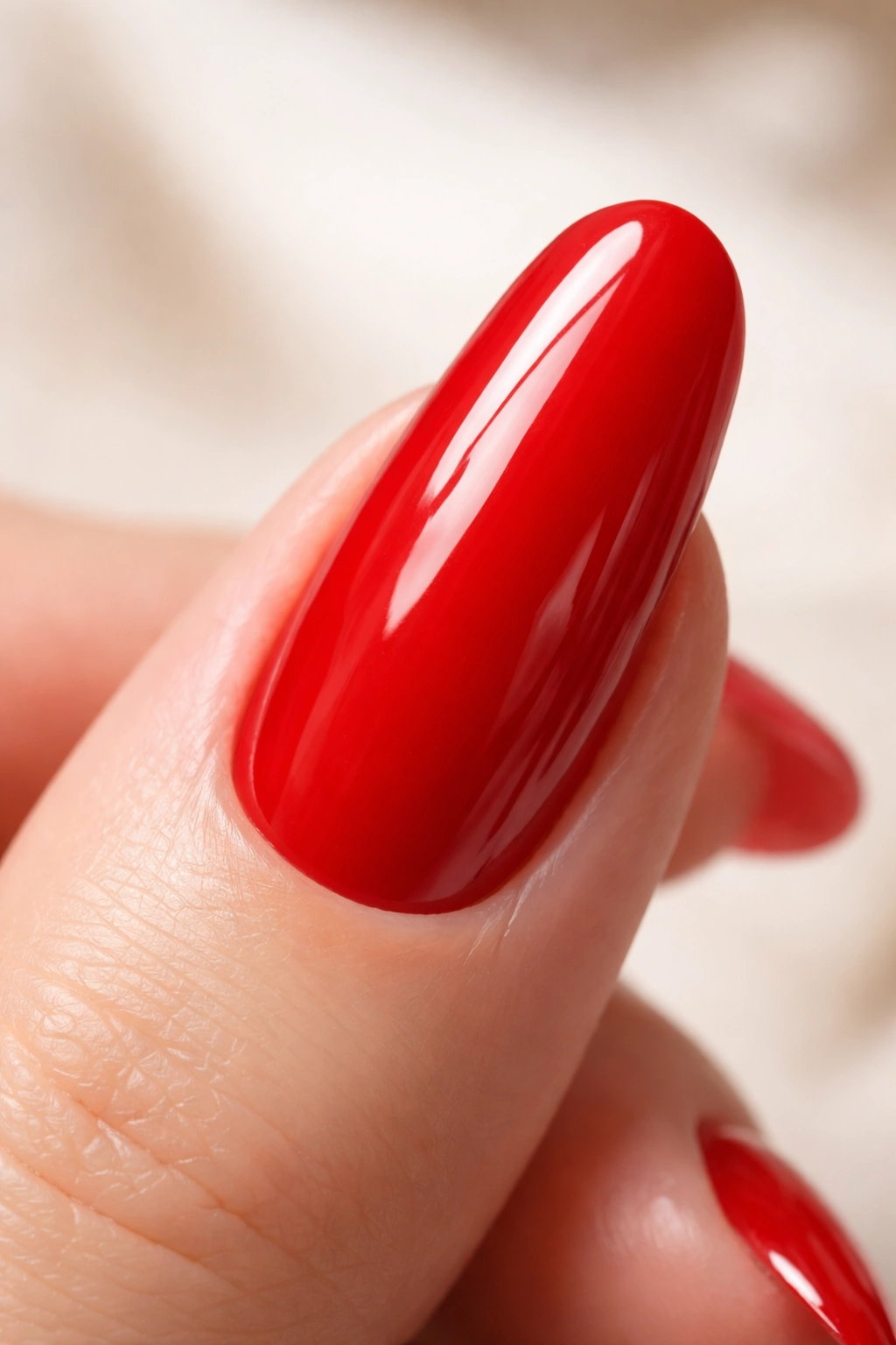 Close-up of a glossy red round acrylic nail on a neutral background