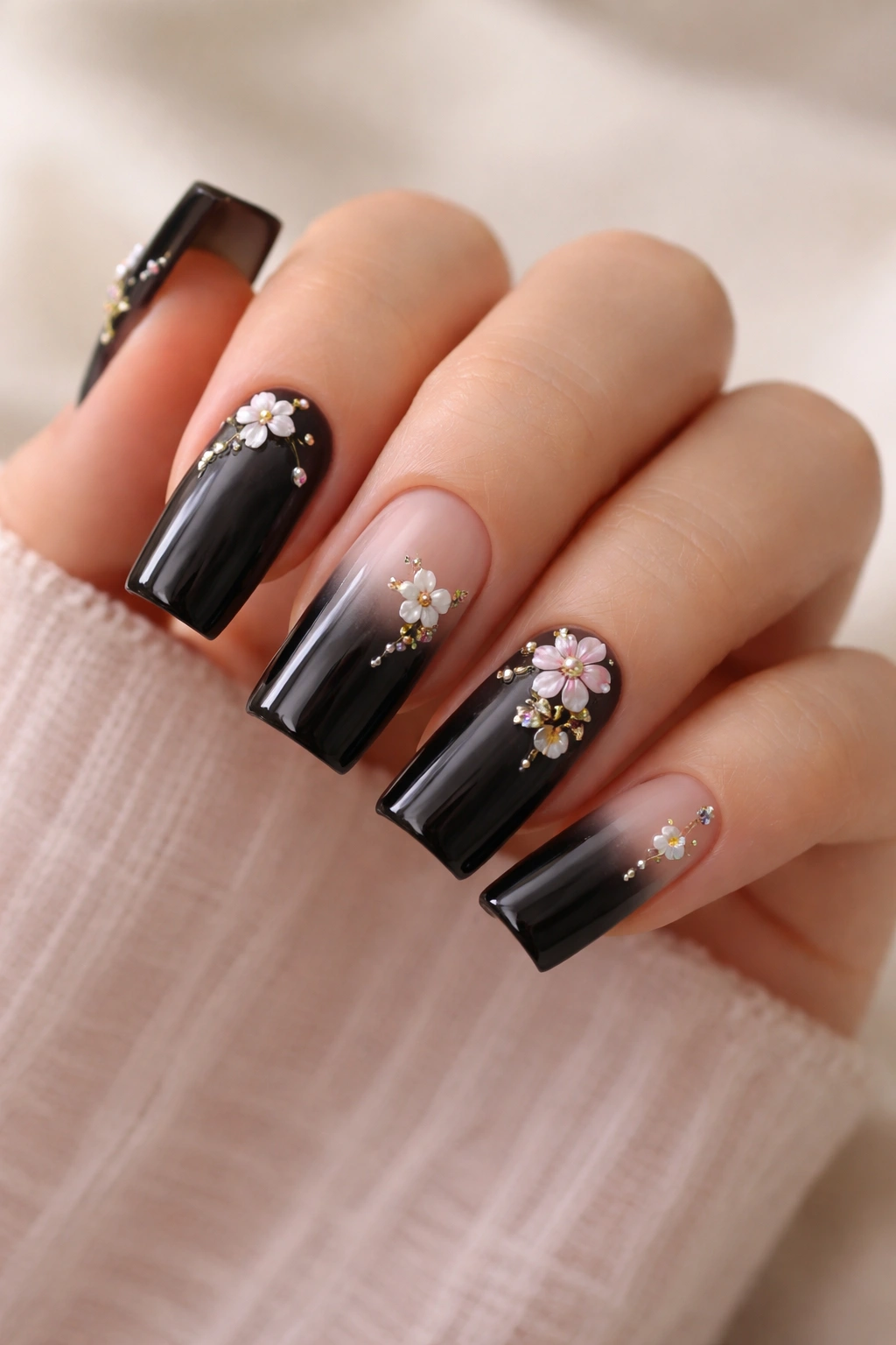 Nails with small floral charms on a black gradient