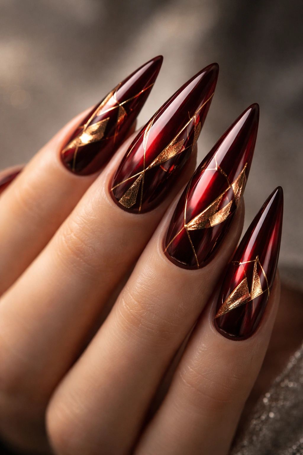 Dark red stiletto nails with foil accents and geometric shapes close-up