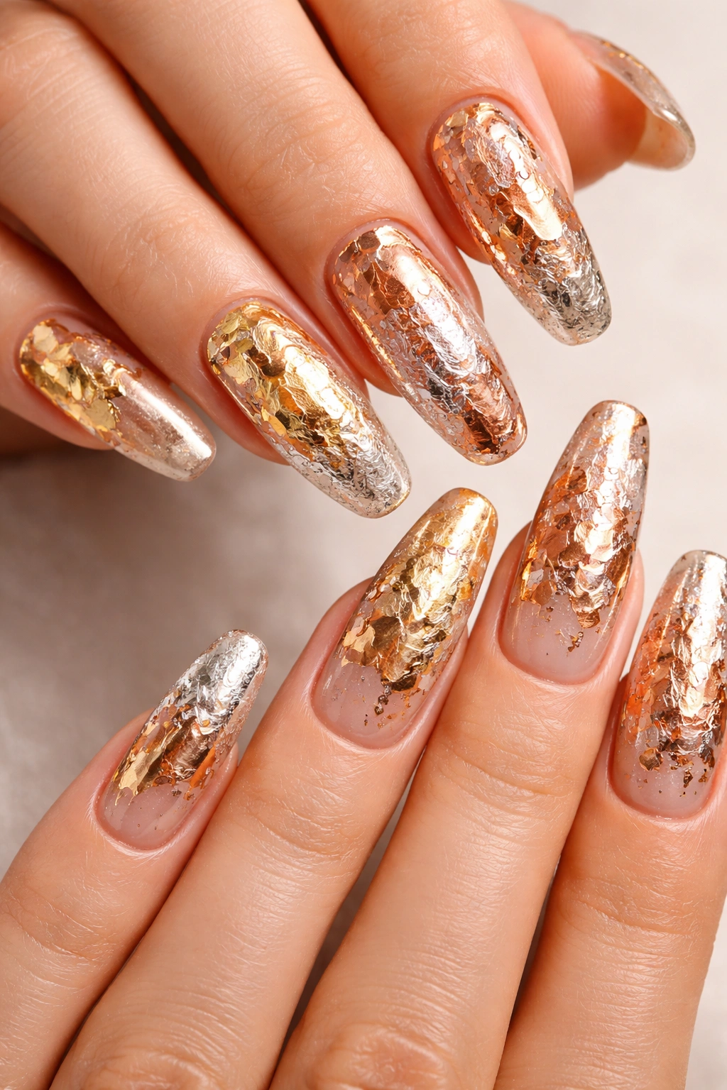 Close-up of long nails with irregular metallic foil accents in gold and copper