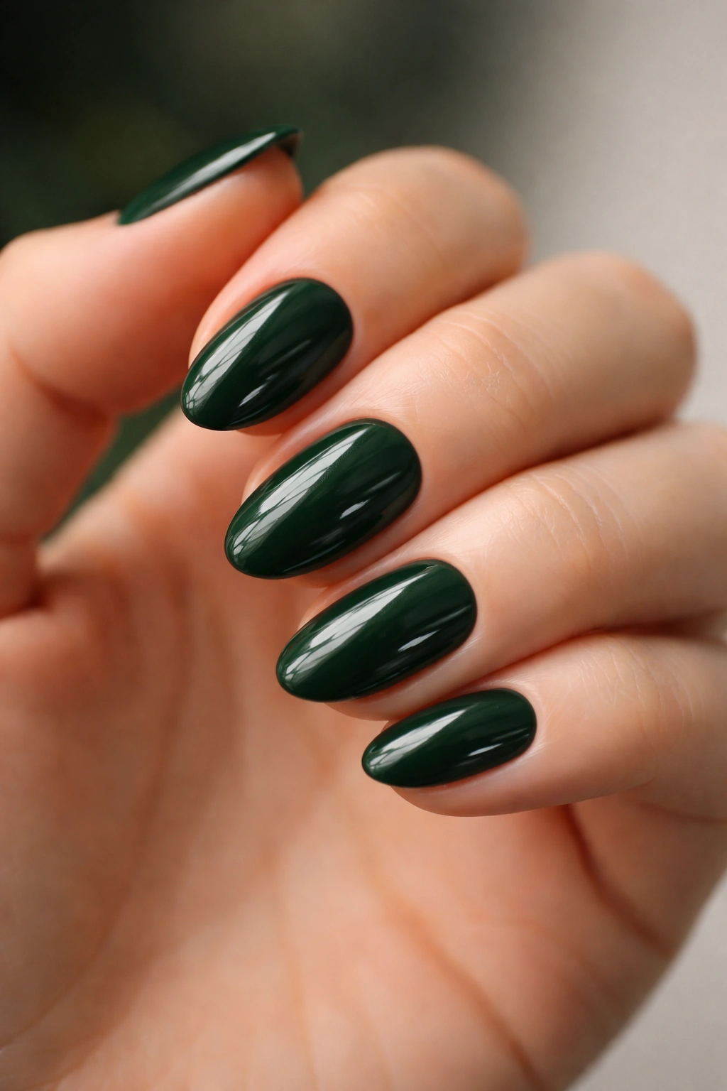 Close-up of short almond nails in forest green with glossy jewel-like finish