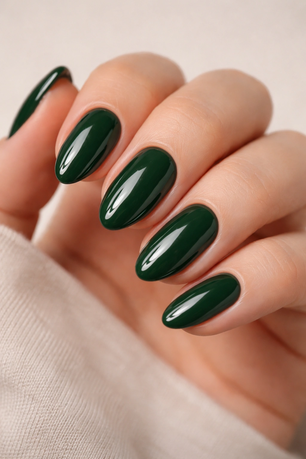 Close-up of short almond nails in glossy forest green, highlighting curved nails and rich shine.