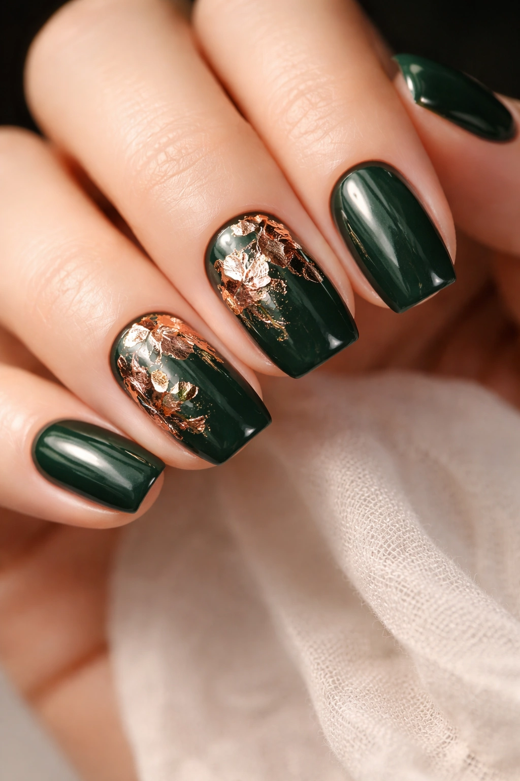 Close-up of forest green crème squoval nails with rose gold foil leaves for dimensional texture
