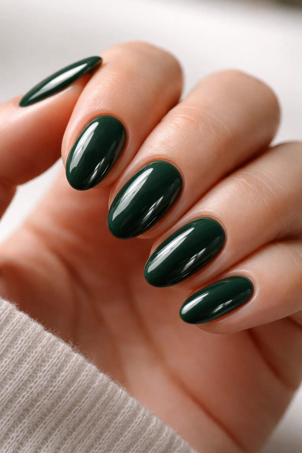 Close-up of short almond nails in deep forest green with a high-gloss finish.