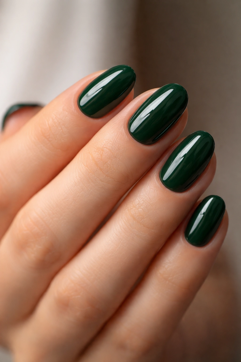 Close-up of short oval nails painted deep forest green with a jewel-toned gloss