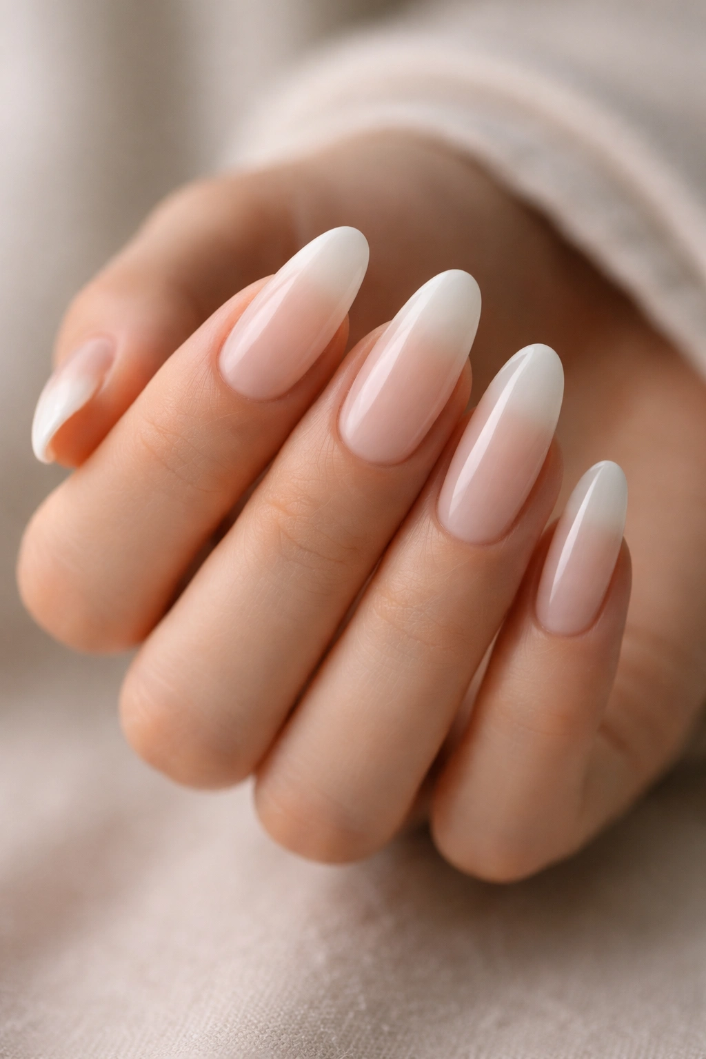 Long oval nails with milky French ombre and soft cream edges on a neutral background