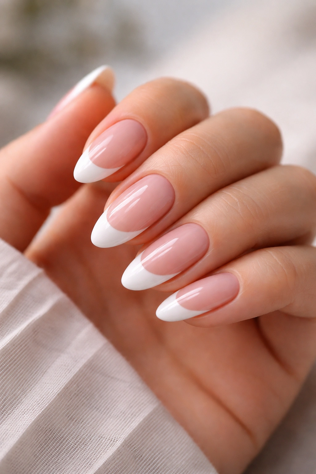 Close-up of an almond-shaped French tip manicure with white tips on a pink base
