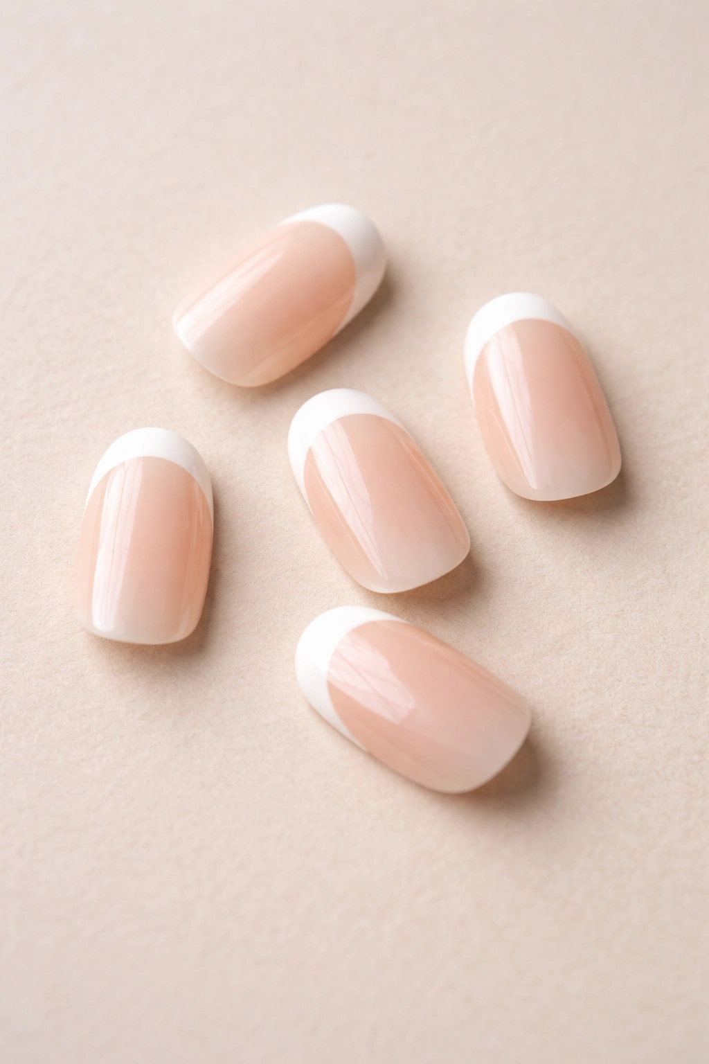 Close-up of five short oval nails with French tips on a neutral surface