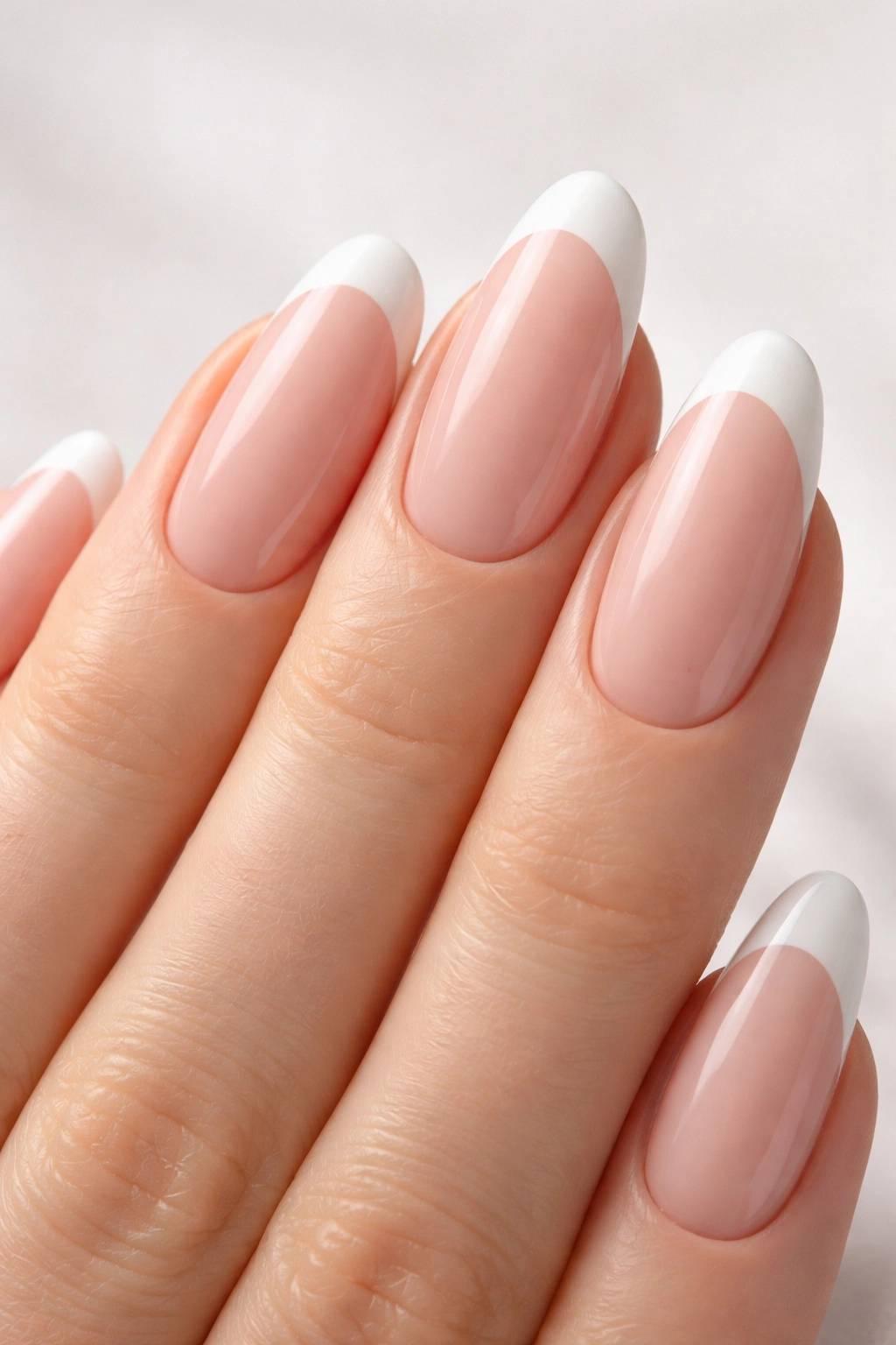 Close-up of long oval nails with soft pink base and white French tips, glossy finish