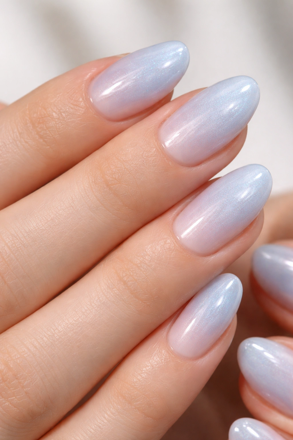 Close-up of very short almond nails with sheer frosted blue over a milky base and subtle shimmer