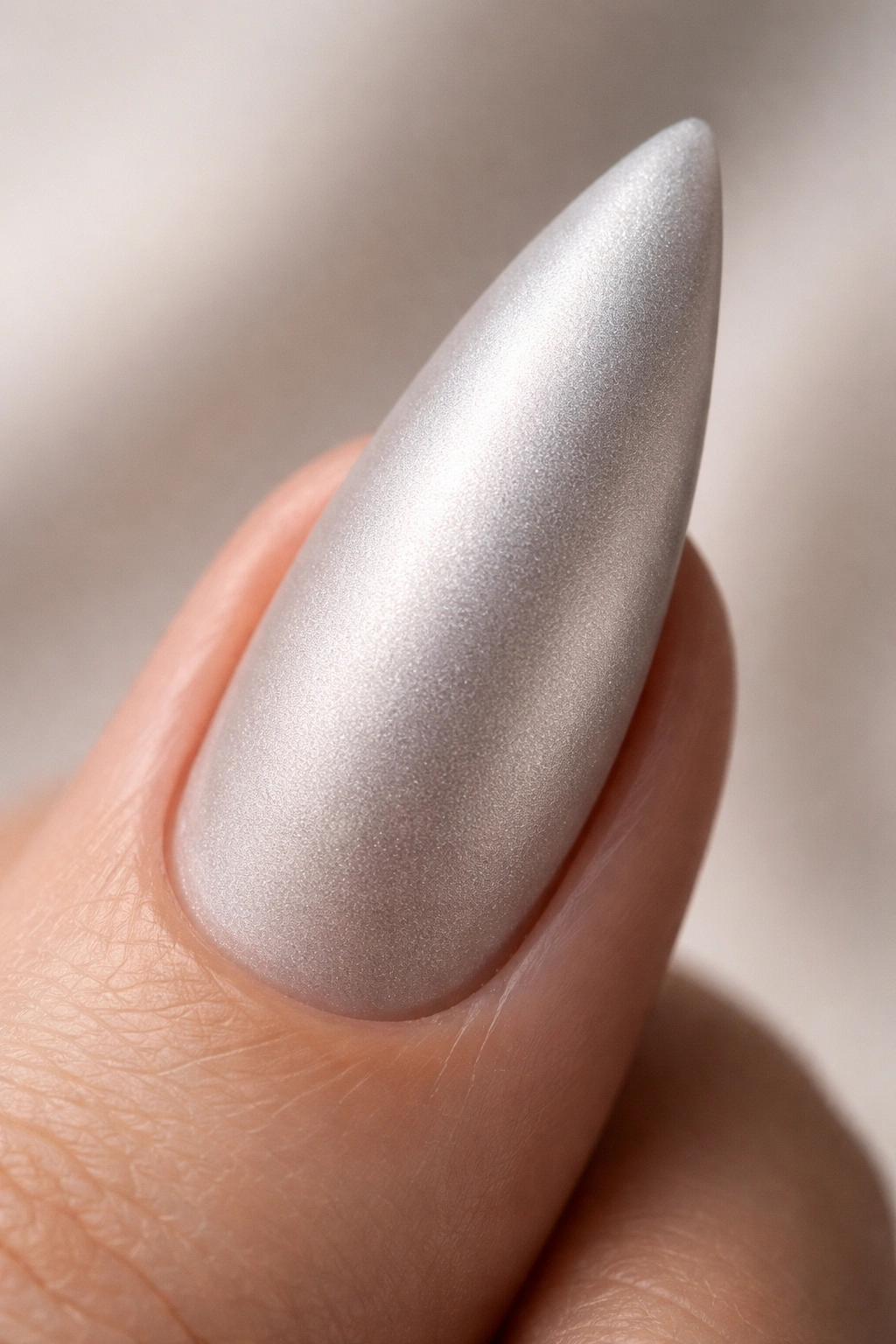 Close-up of frosted silver stiletto nail with matte finish.