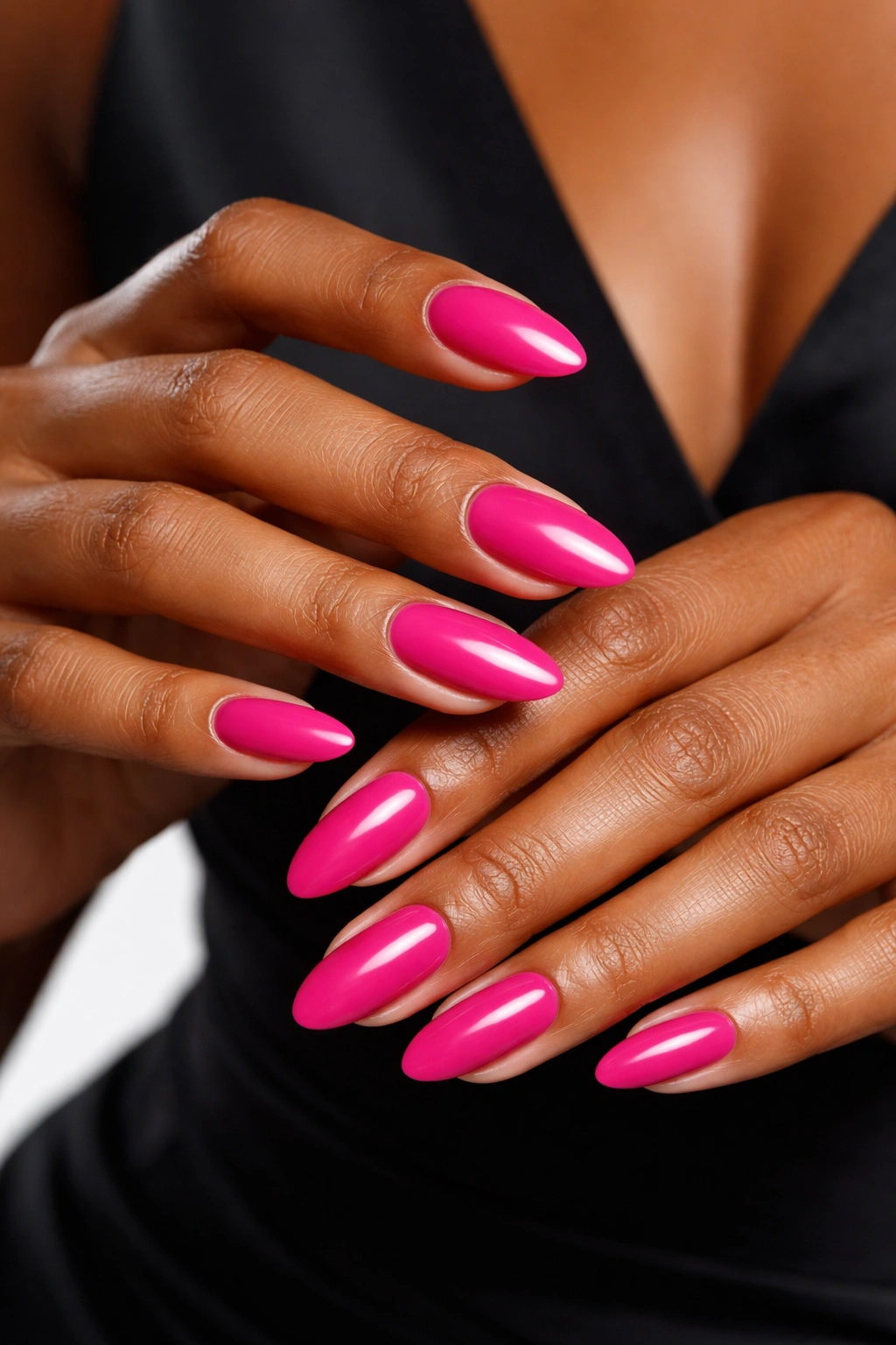Close-up of nails painted bold fuchsia on hands against a neutral backdrop