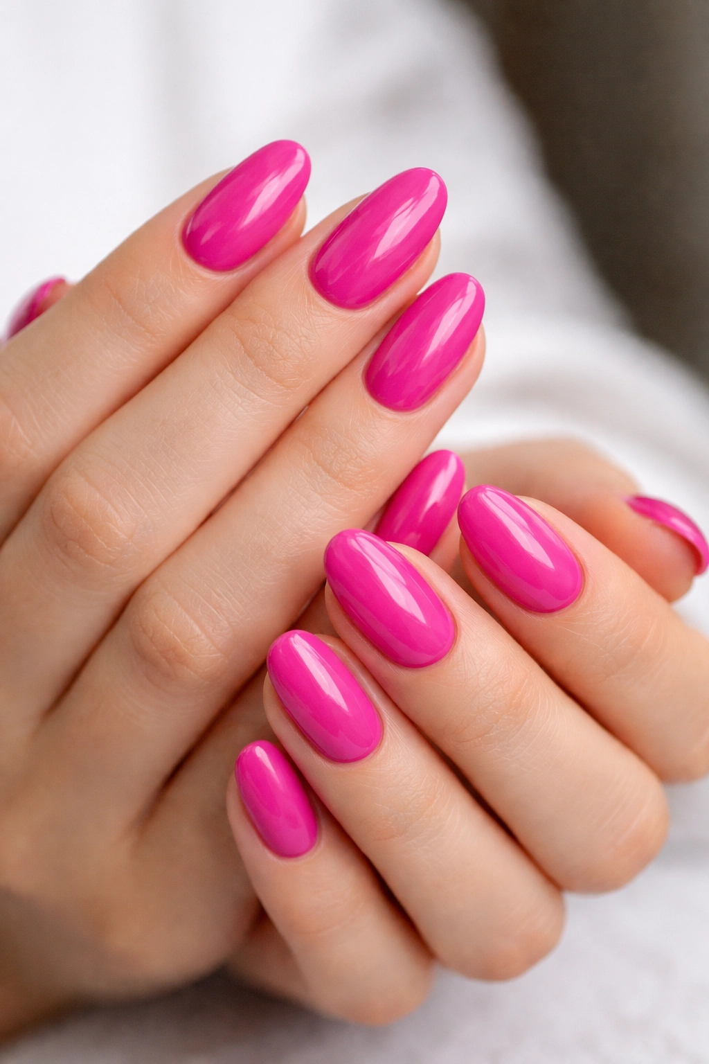 Close-up of short almond nails painted in cool-toned fuchsia with gloss.
