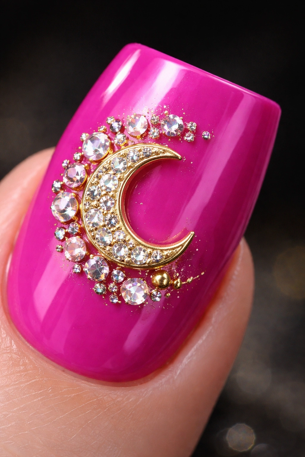 Close-up of fuchsia nail with gold crescent charm and rhinestones.