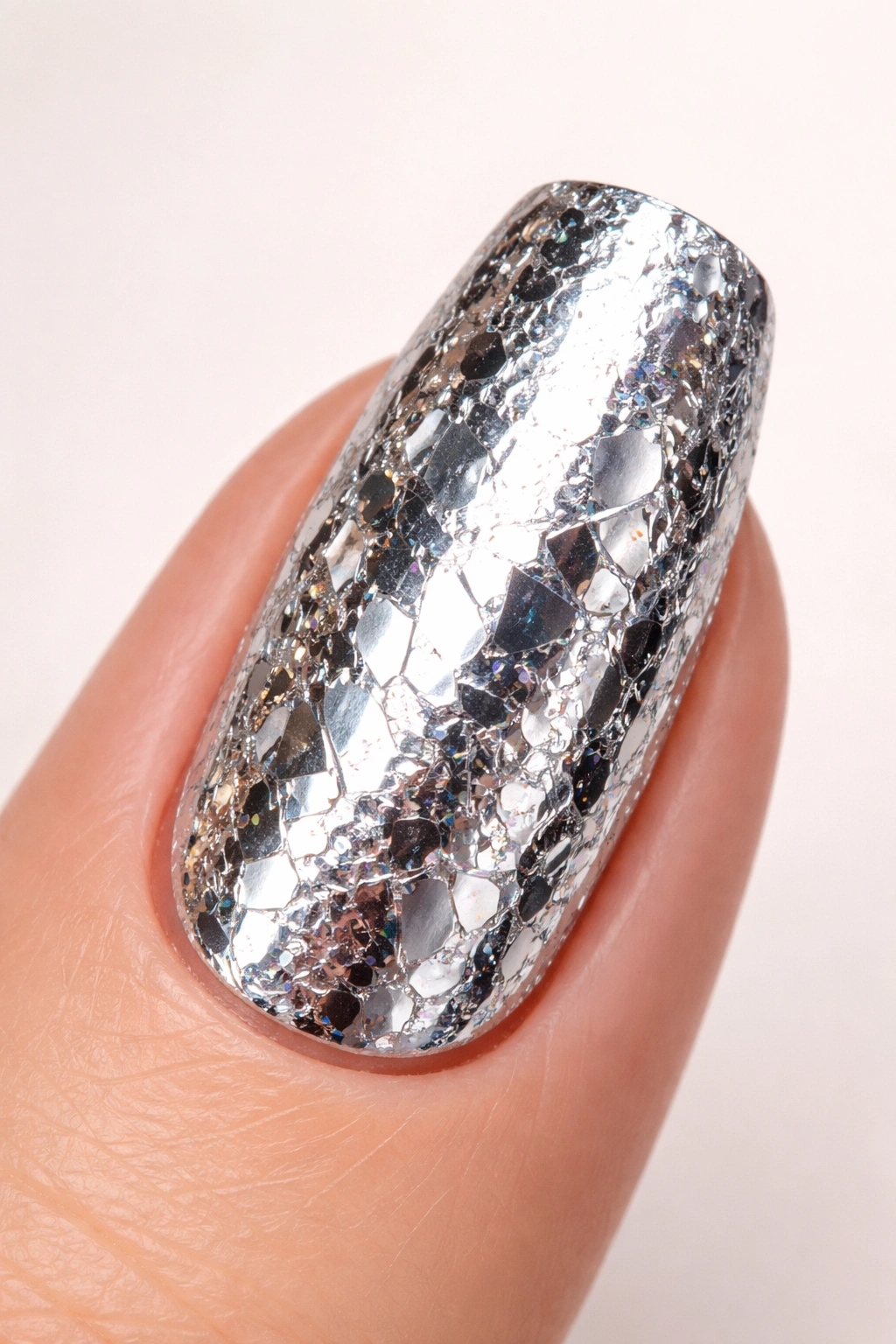 Close-up of a nail fully coated in foil with high shine on a neutral background.