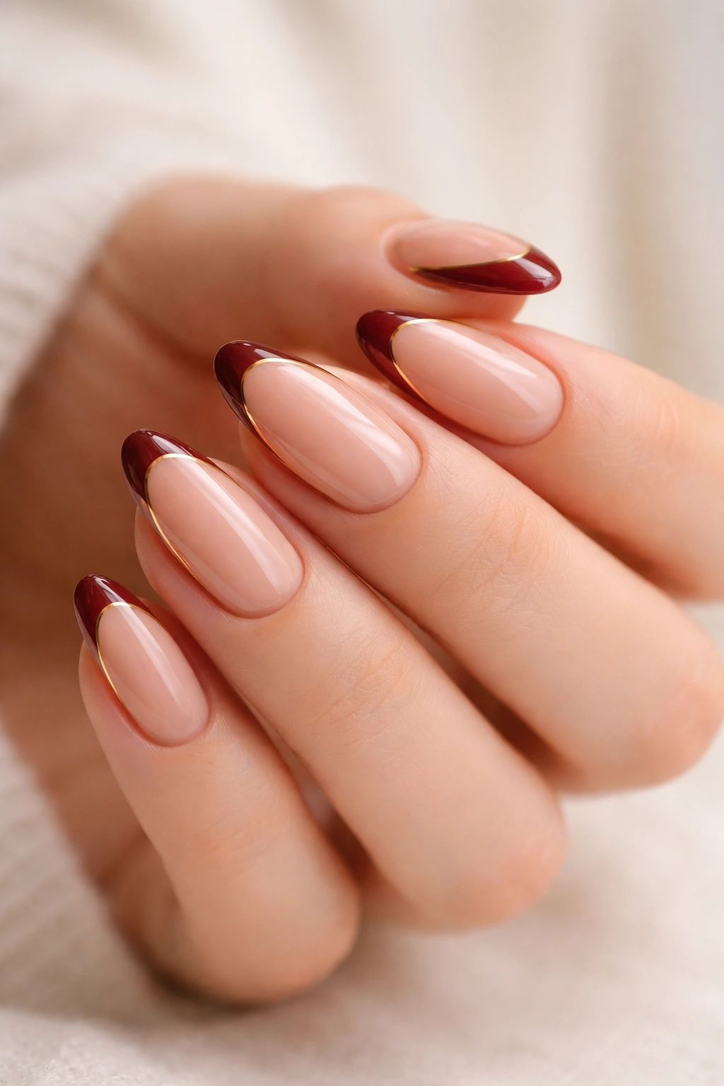 Close-up of almond nails with garnet tips and thin gold outline