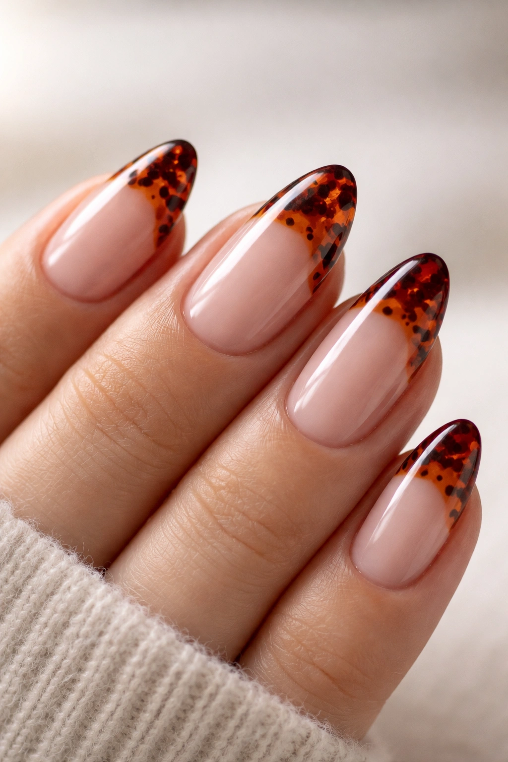 Close-up of a short almond nail with garnet red tortoiseshell pattern on the tip