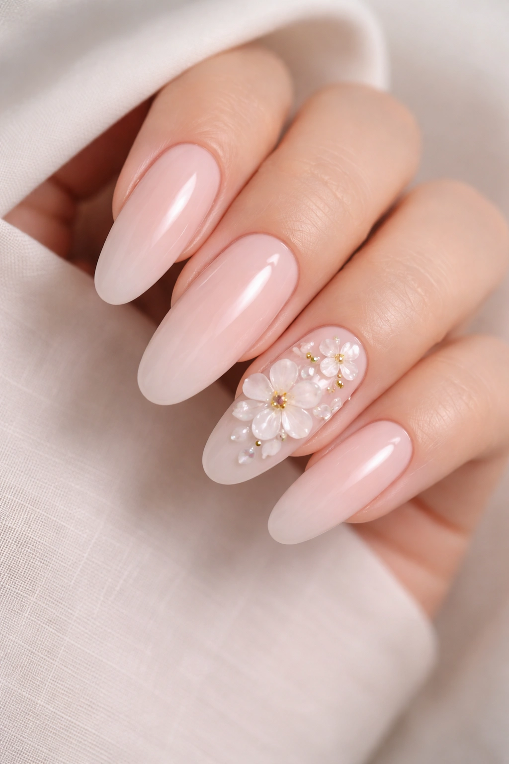 Close-up of long oval nails with 3D gel flowers on accent nails against a soft blush base