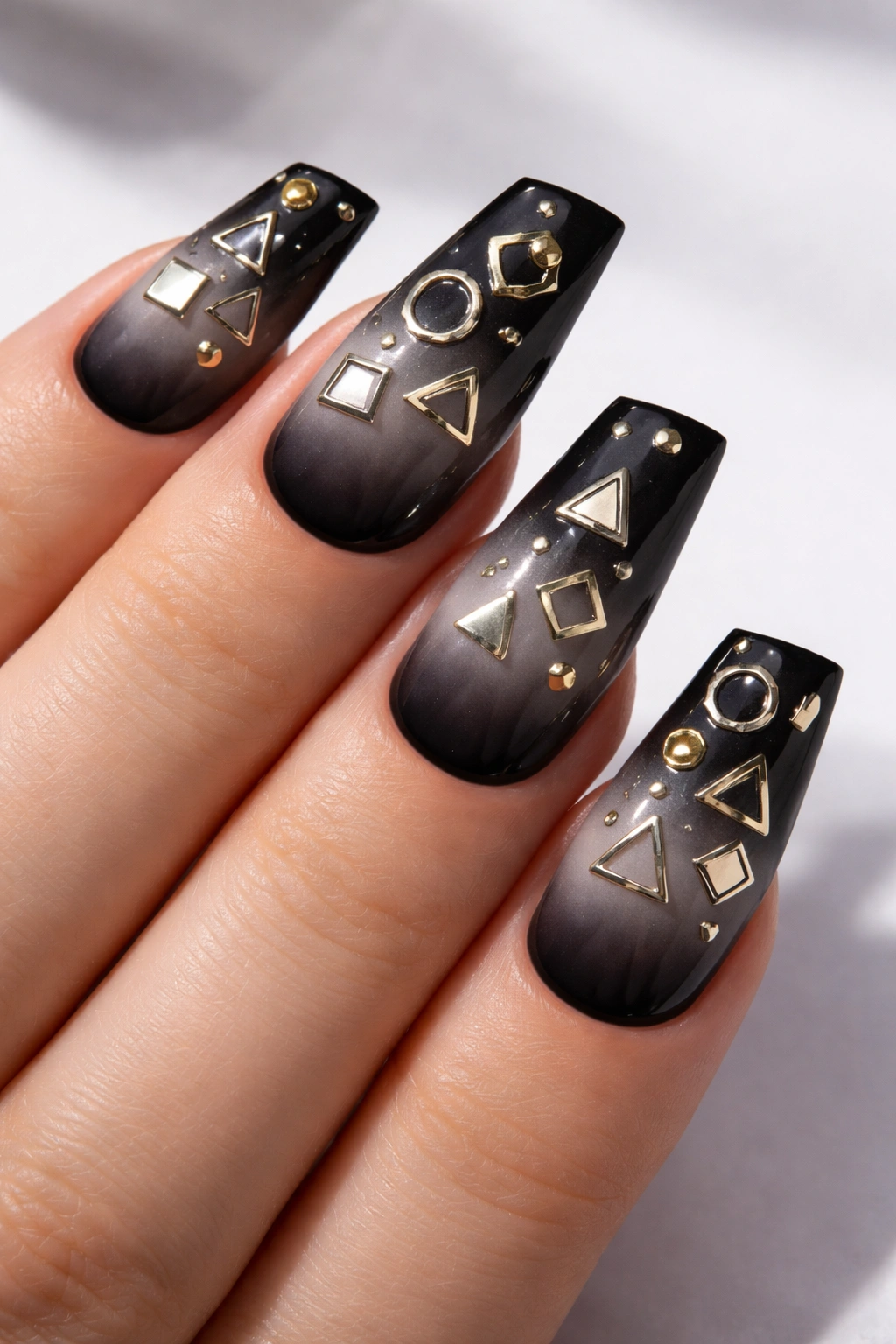 Close-up of black duck nails with mixed gold and silver geometric charms on stiletto tips