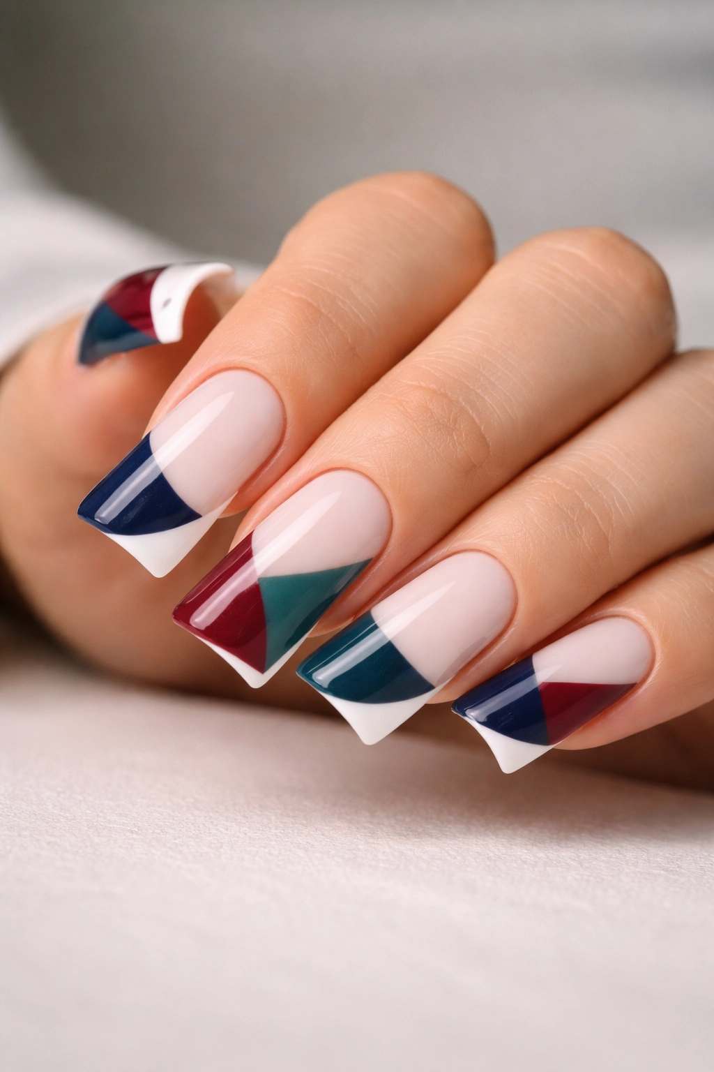 Close-up of duck nails with color-blocked geometric French tips in navy, burgundy, and teal.